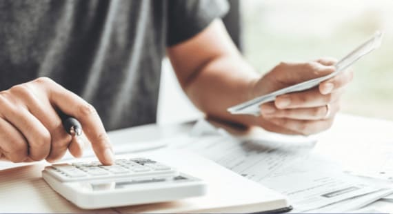 A mans hands looking at a calculator and a sheet of paper for finances