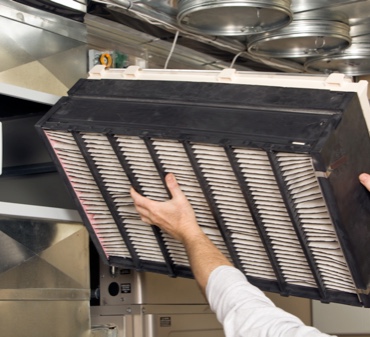HVAC Technicion in a white shirt replacing an industrial air filter in a commercial kitchen