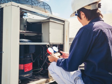 HVAC Technicion in a blue shirt and white hat doing preventative maintenance on a rooftop HVAC unit